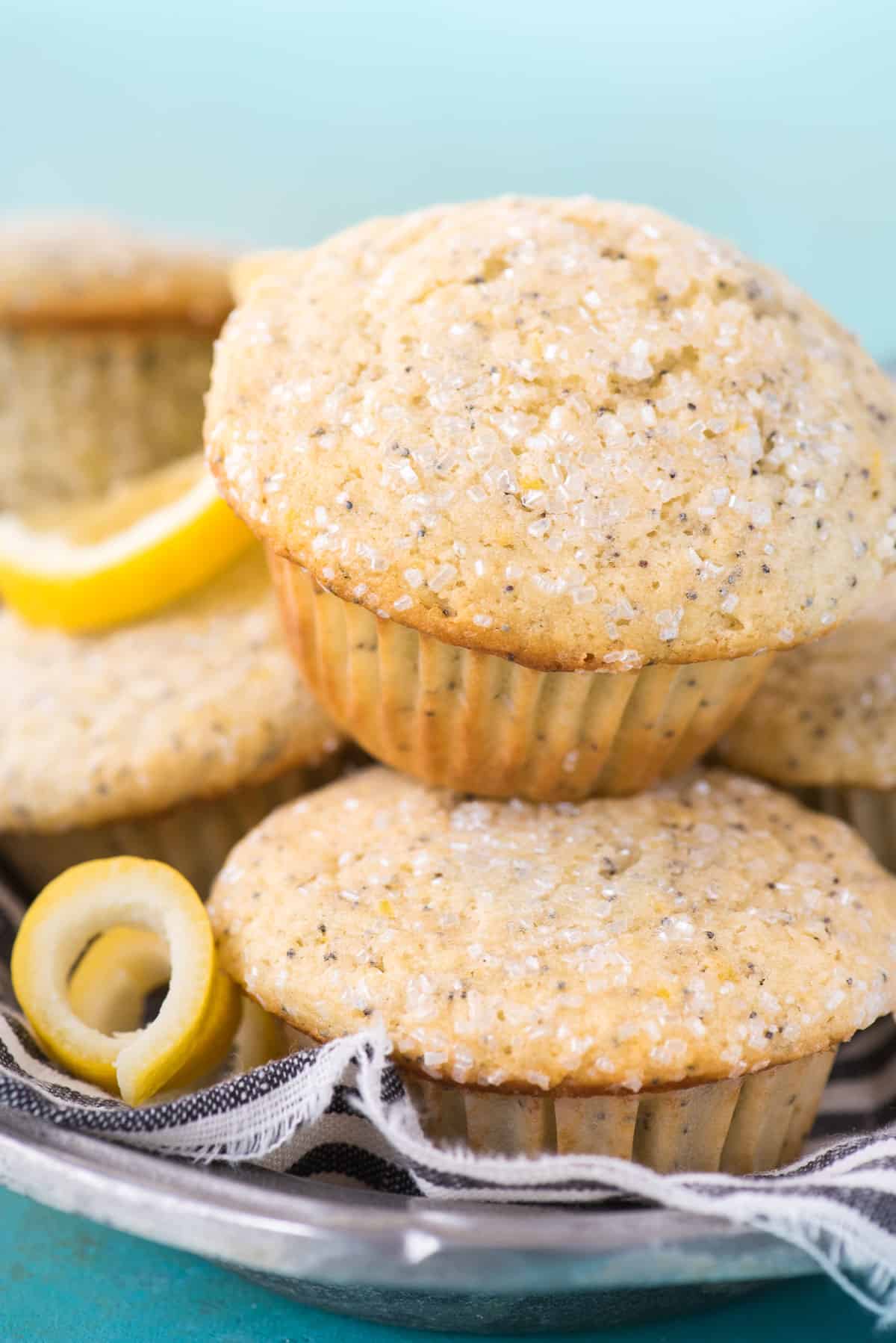 lemon poppy seed muffins stacked on top of each other in metal dish with blue striped cloth