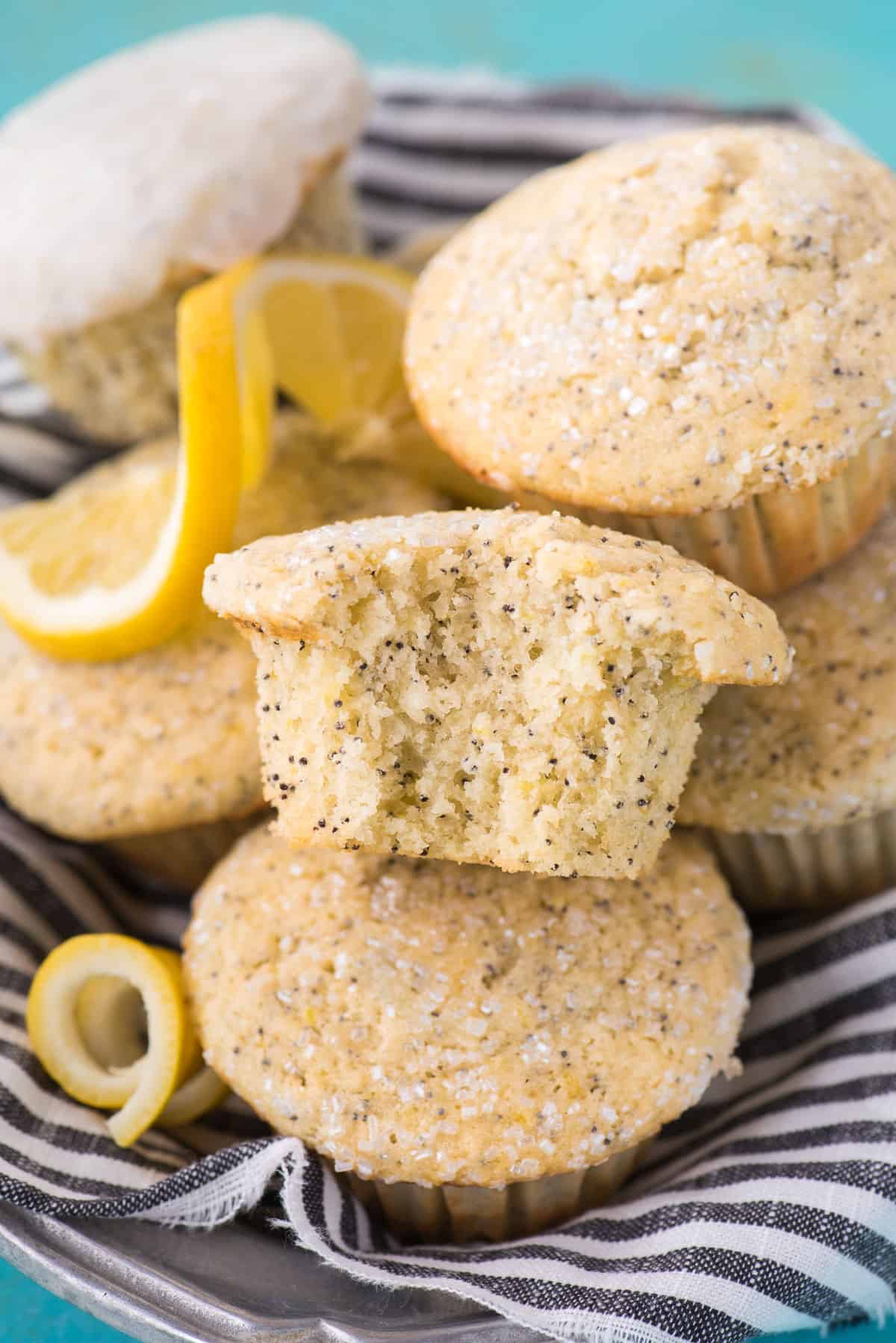 lemon poppy seed muffins stacked on top of each other in metal dish with blue striped cloth