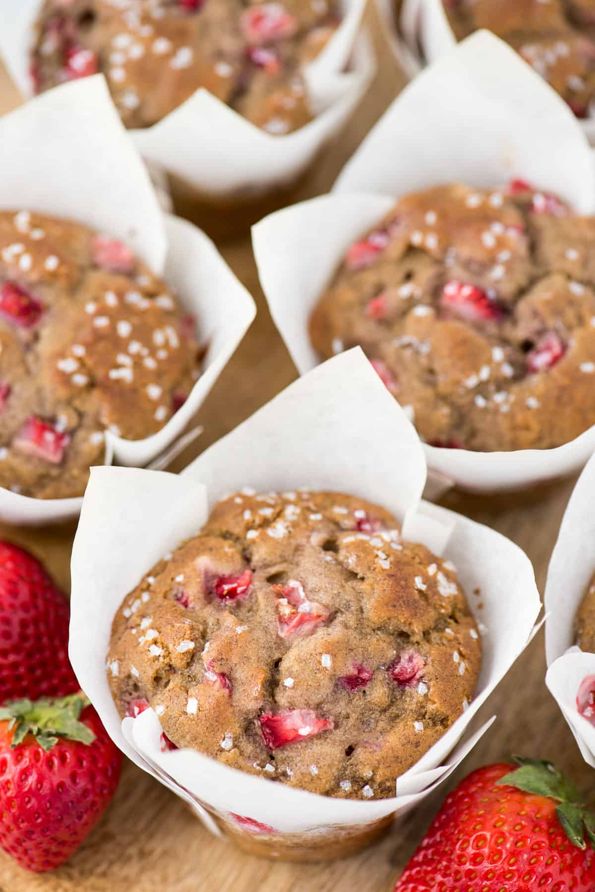 strawberry banana muffins in white parchment paper liners on wooden background