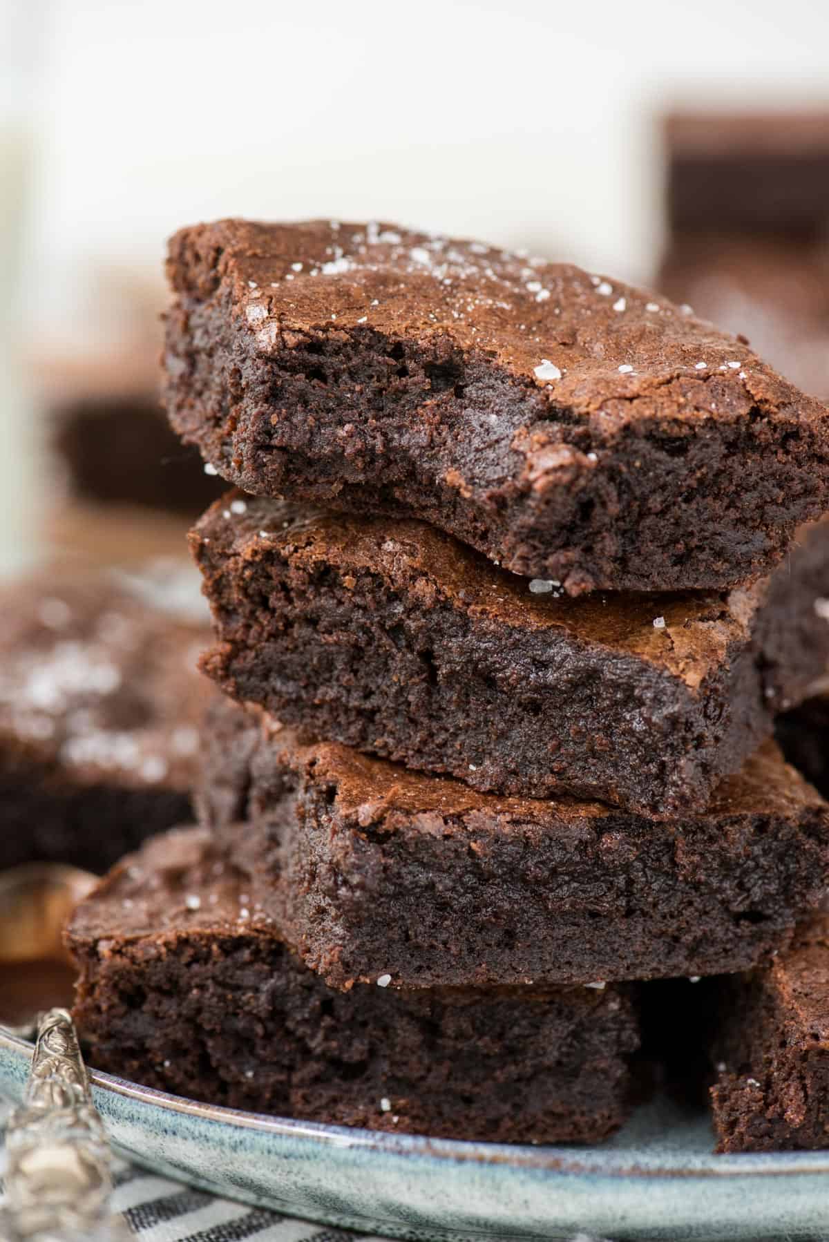 homemade brownies stacked in a tower on light blue plate with white background 