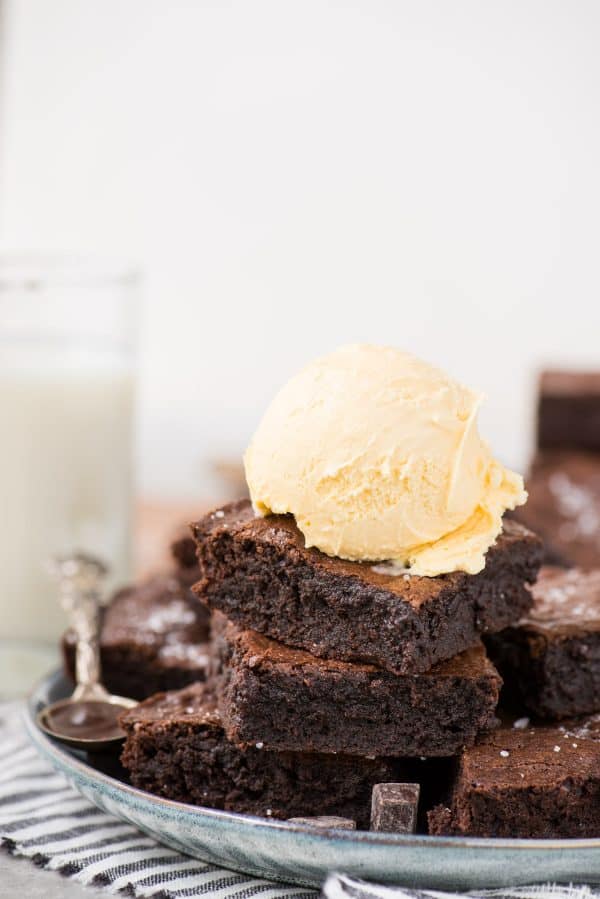 homemade brownies stacked in a tower with single scoop of vanilla ice cream on top on light blue plate with white background