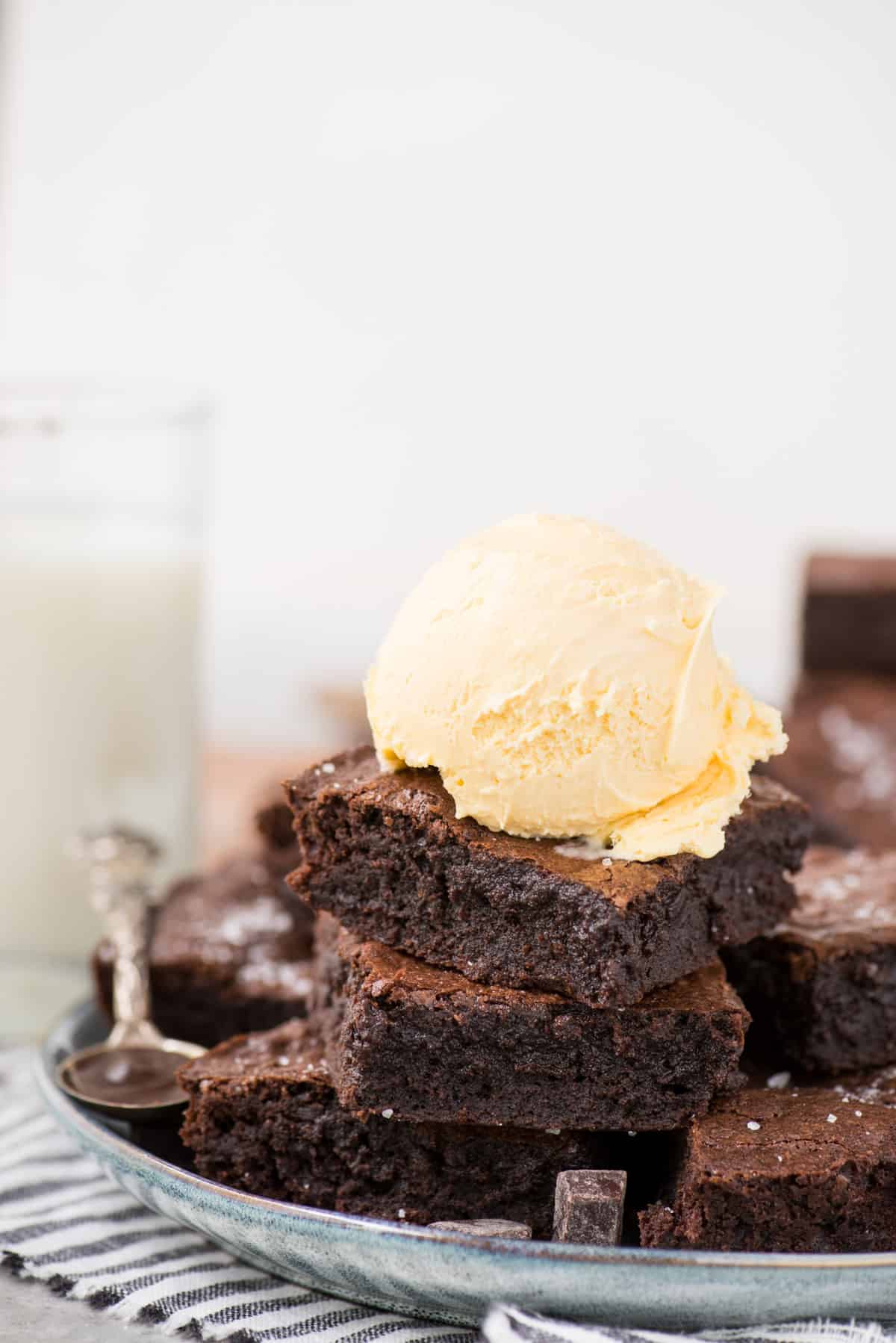  homemade brownies stacked in a tower with single scoop of vanilla ice cream on top on light blue plate with white background 