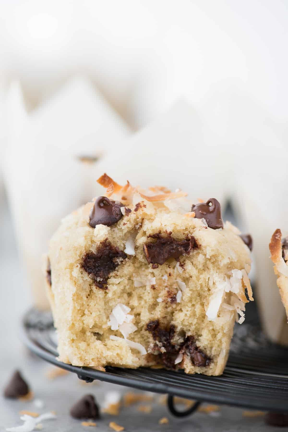 Coconut chocolate chip muffin with bite taken out of muffin on black wire cooling rack