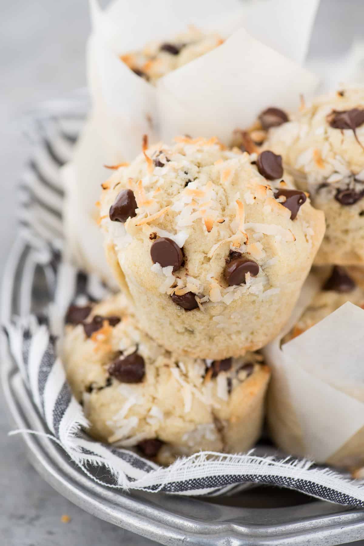 Coconut chocolate chip muffins stacked in a tower on metal platter with blue and white stripe towel