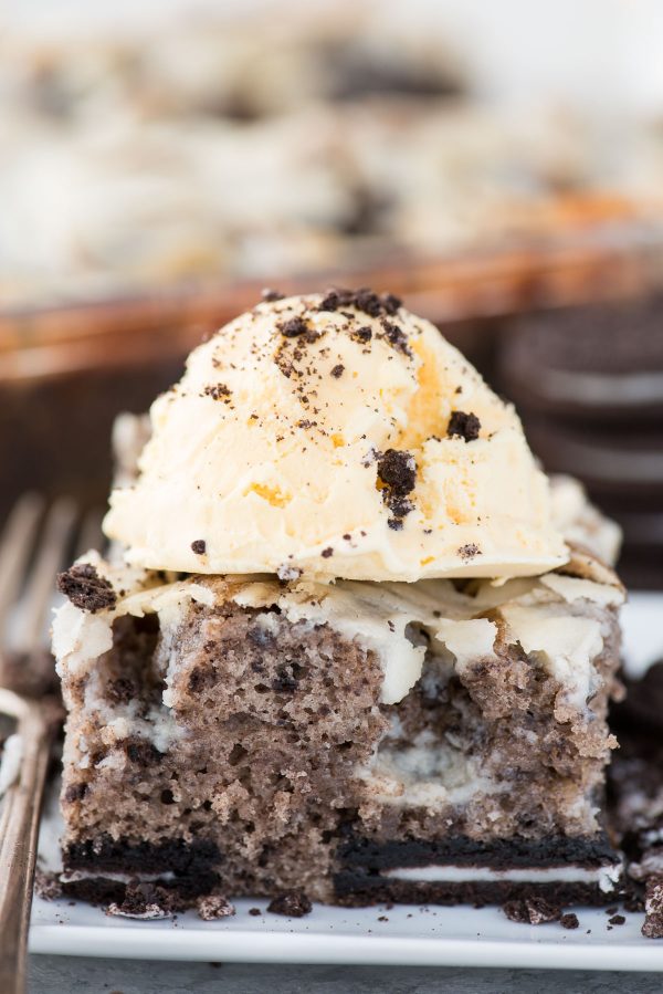 This oreo earthquake cake is a white cake mix loaded with whole oreos and oreo crumbs. Swirl in the cream cheese frosting layer and it bakes into the cake creating frosting filled crevices and cracks on top of the cake. #earthquakecake #oreocake #cake slice of oreo earthquake cake with scoop of vanilla ice cream on top on white plate