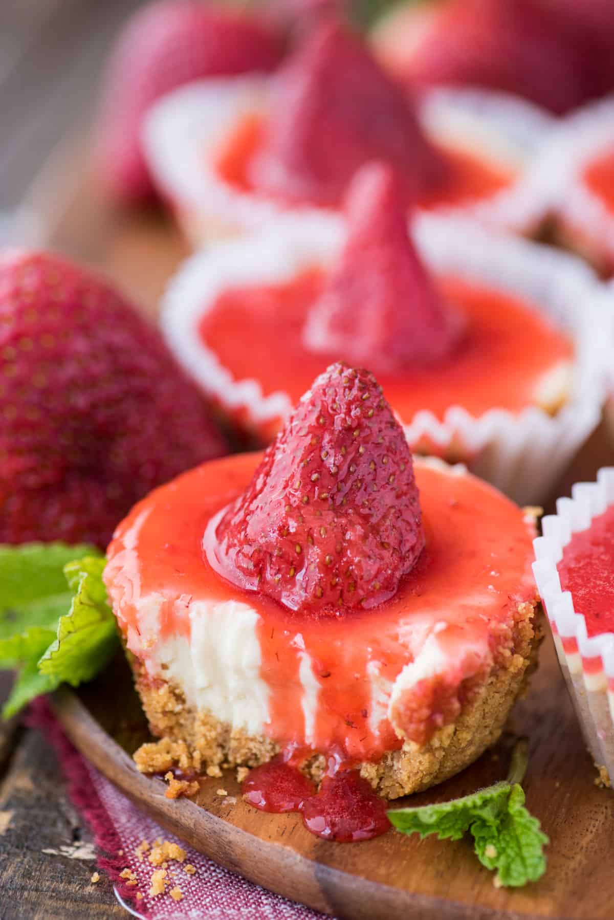 mini plain cheesecake with bite removed with strawberry topping on wood serving tray