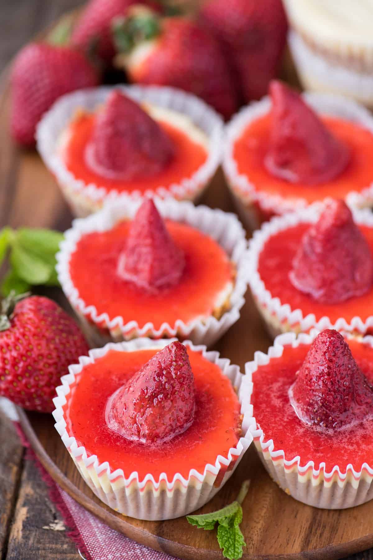 6 mini plain cheesecakes with strawberry topping on wood serving tray