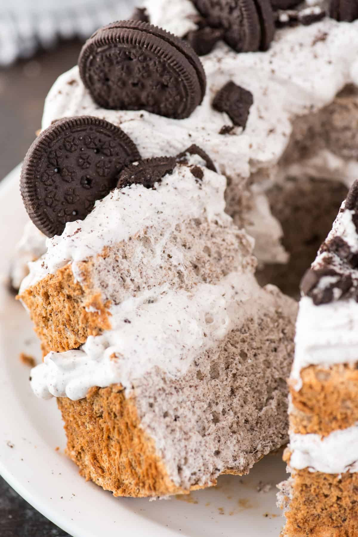 slice of oreo angel food cake with oreo whipped cream and crushed oreo pieces on white plate on dark background