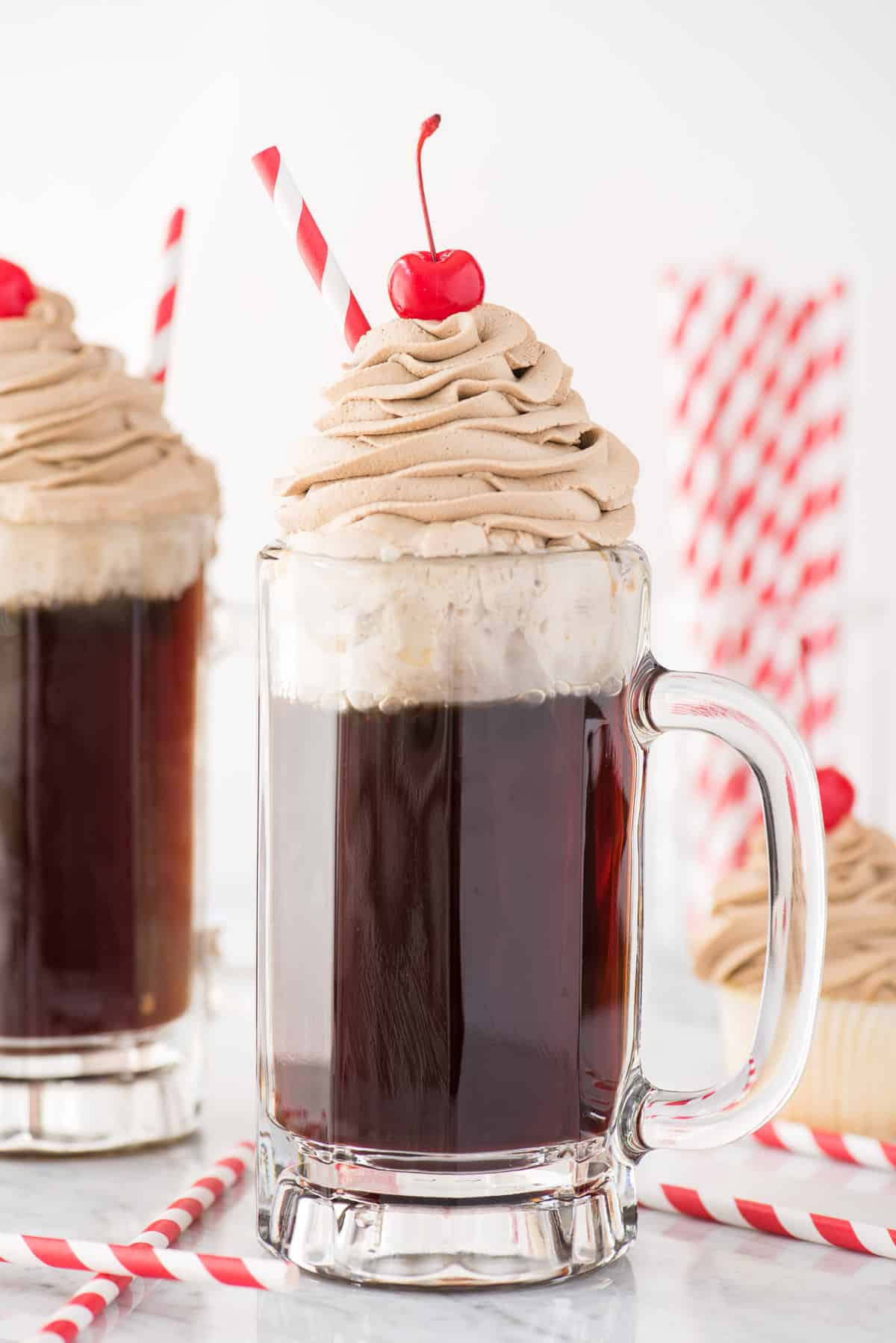 root beer whipped cream piped on top of root beer in a mug with maraschino cherry and red straw