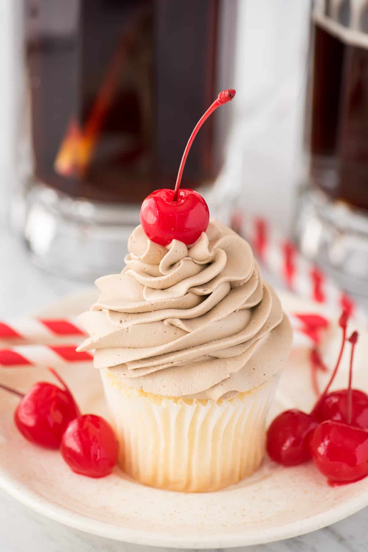 root beer whipped cream on top of white cupcake with maraschino cherry on white plate