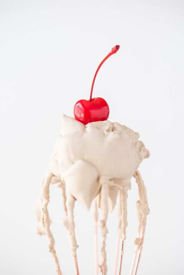 root beer whipped cream with maraschino cherry on a rose gold whisk