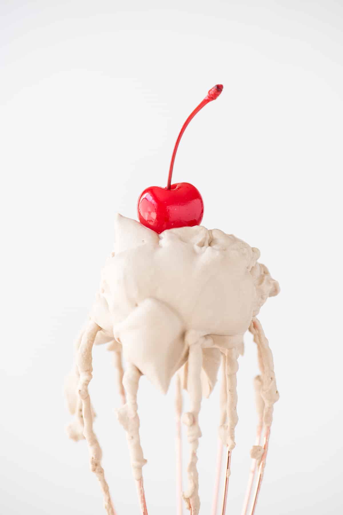 root beer whipped cream with maraschino cherry on a rose gold whisk