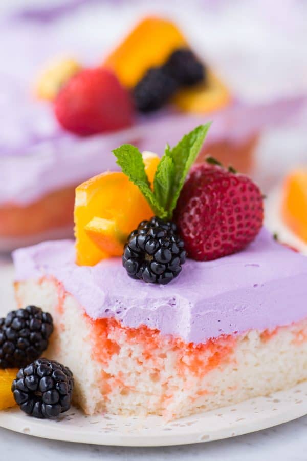 slice of sangria poke cake garnished with a strawberry, blackberries, orange slice and mint leaf on white plate