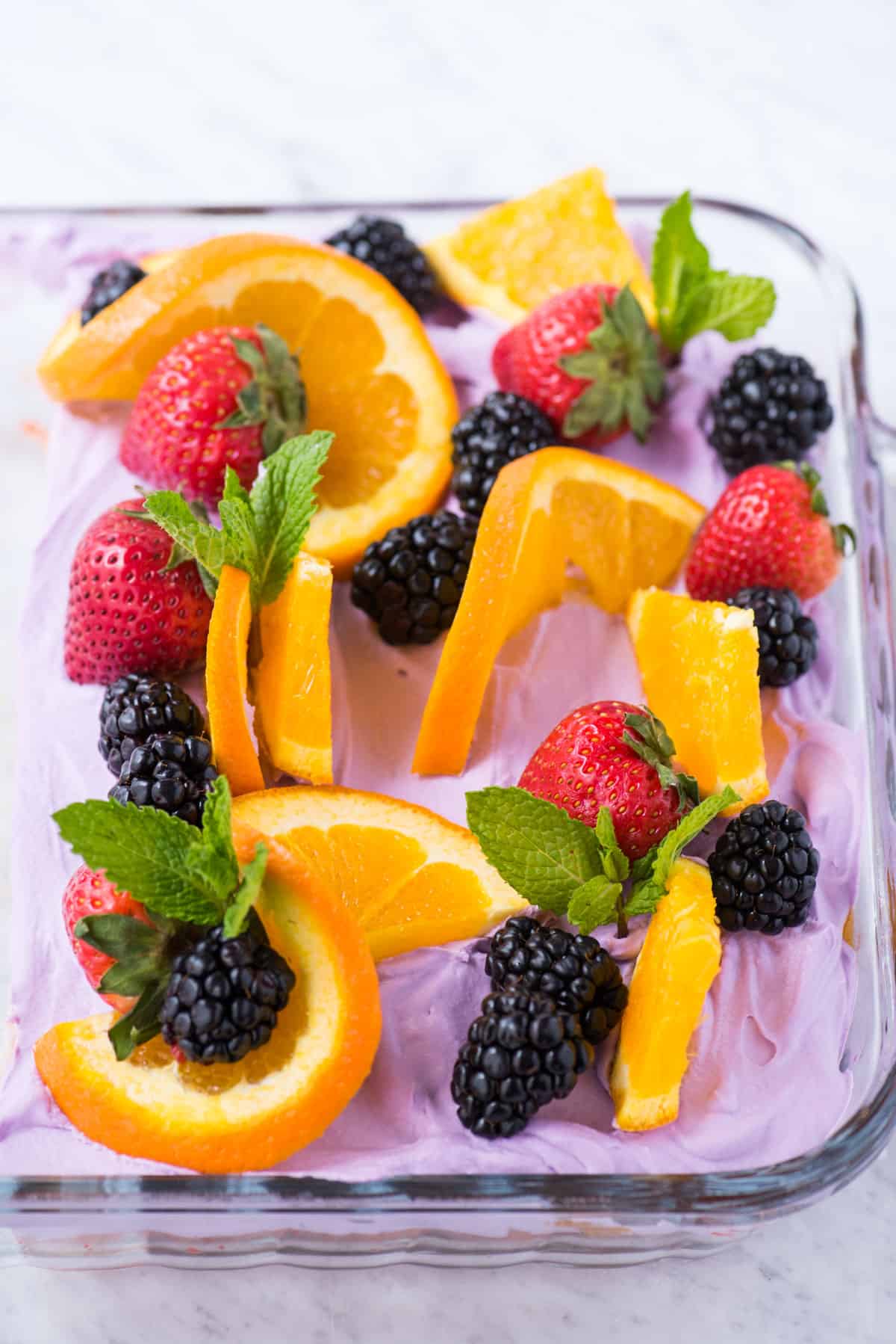 sangria poke cake decorated with orange slices, strawberries, blackberries and mint leaves in a glass pan