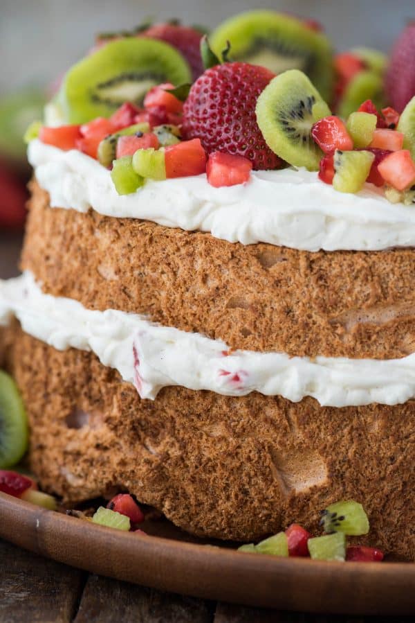close up image of the side of strawberry angel food cake with whipping cream, strawberries and kiwi