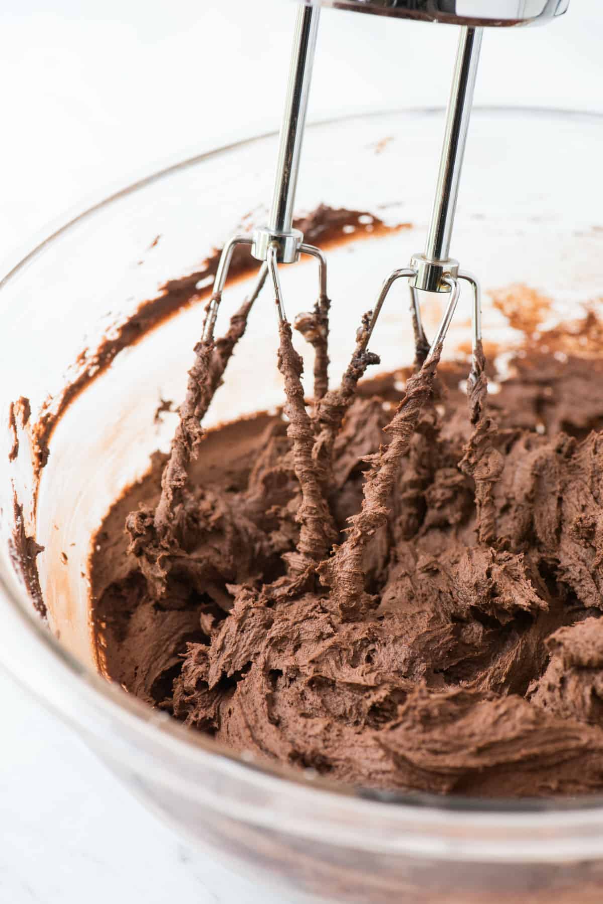 chocolate frosting in glass mixing bowl with electric mixer