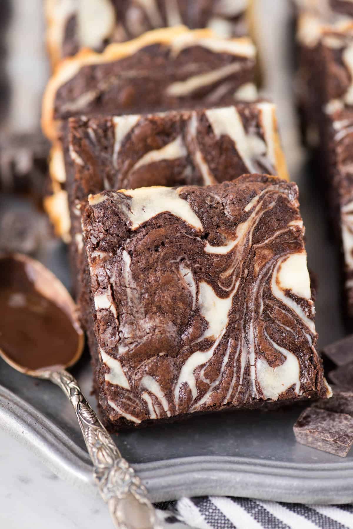 cream cheese swirl brownie on metal serving tray with spoon dipped in chocolate