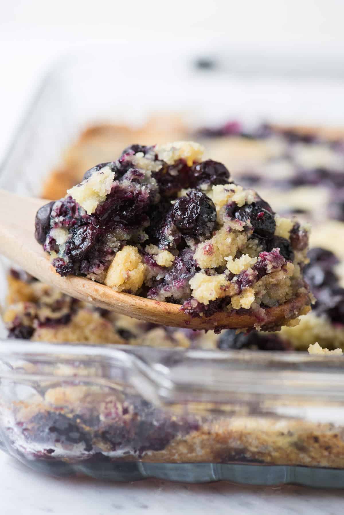 lemon blueberry dump cake in glass 9x13 inch pan with wooden spoon scooping some out