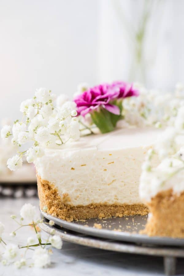 side shot of no bake cheesecake with white and pink flowers on white marble background