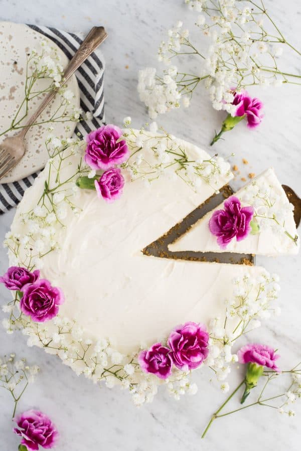 aerial view of whole no bake cheesecake with white and pink flowers on white marble background with one slice slightly removed