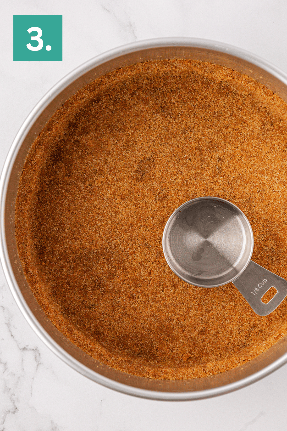A metal bowl filled with a reddish-brown spice mixture and a metal 1/3 cup measuring cup inside evokes a cozy kitchen, reminiscent of preparing a philadelphia no bake cheesecake. In the top left corner, a green box displays the number 3 in white.