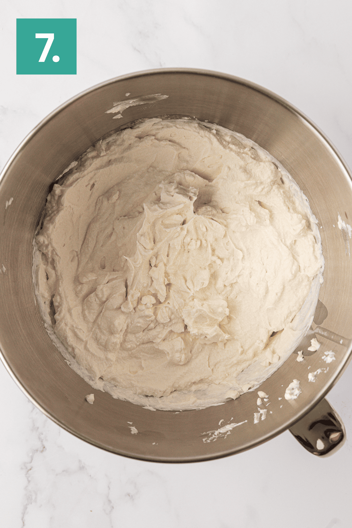 A metal mixing bowl filled with smooth, creamy philadelphia no bake cheesecake batter sits on a white marble surface. A green box with the number 7 is in the upper left corner of the image.