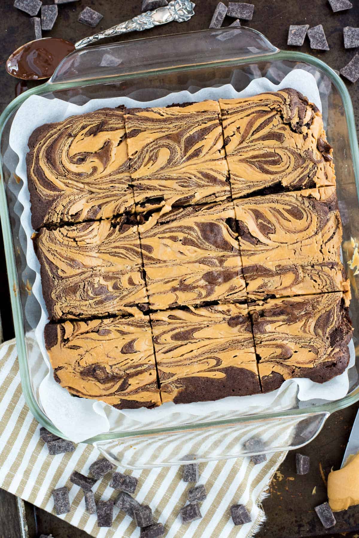 peanut butter swirl brownies cut into squares in glass pan on dark background with cream and tan striped cloth