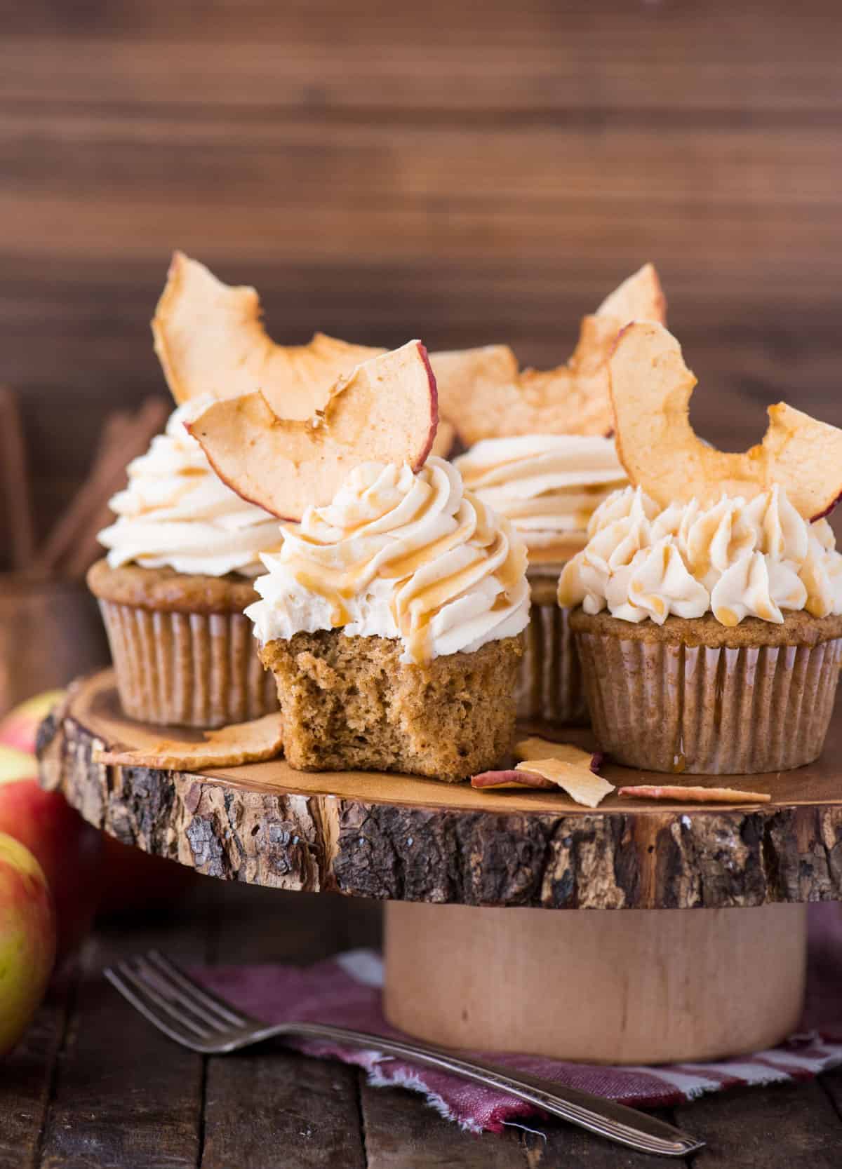apple spice cupcakes with caramel frosting and apple chips on wood cake stand with wood background 