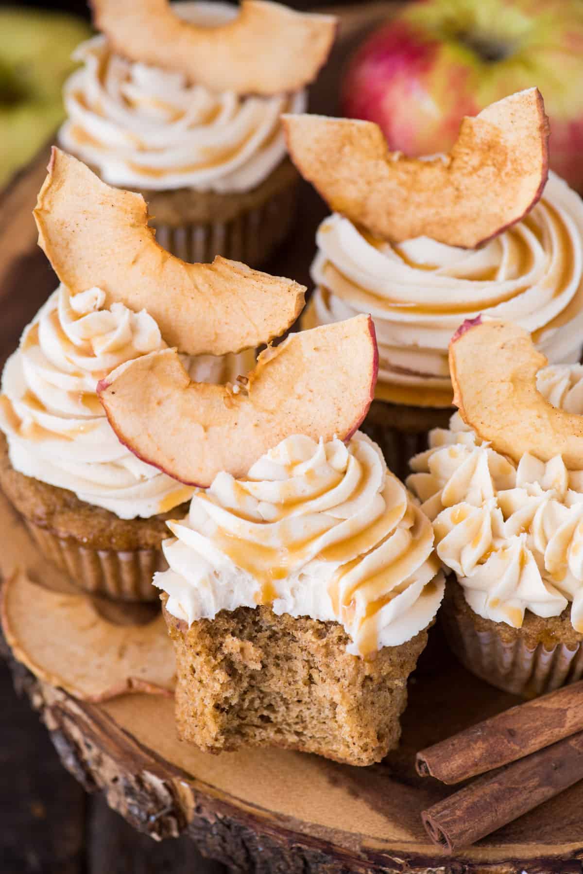 apple spice cupcakes with caramel frosting and apple chips on wood cake stand with wood background