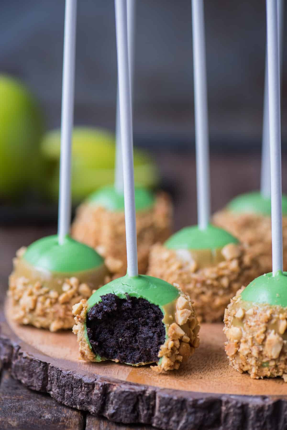 oreo balls that look like caramel apples with bite removed on round wooden stand with metal background