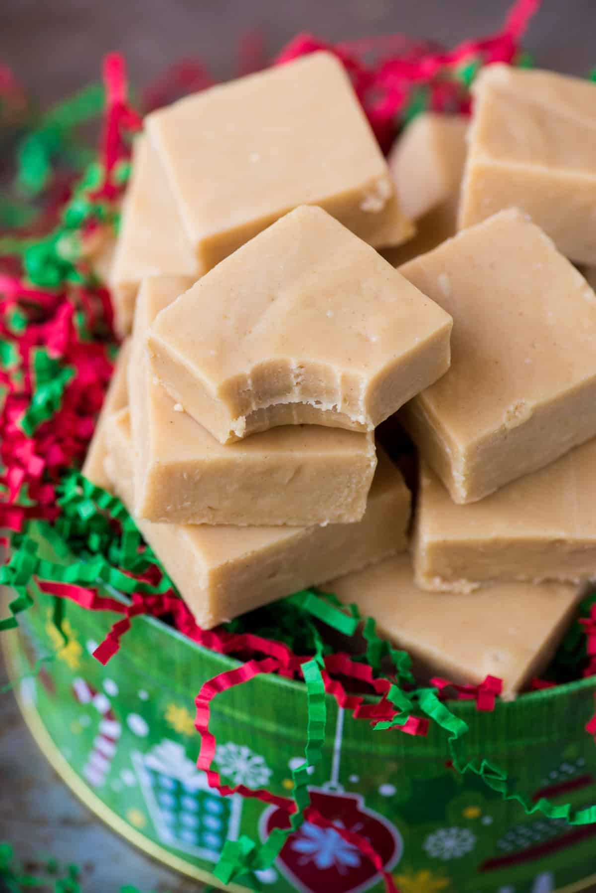pieces of peanut butter fudge inside a christmas tin with red and green crinkle paper