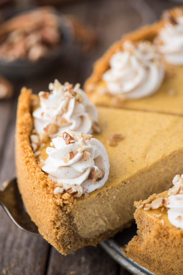slice of pumpkin cheesecake with whipped cream swirls and chopped nuts being removed from cheesecake pan