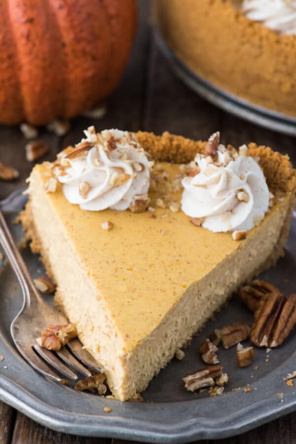 a slice of pumpkin cheesecake with whipped cream swirls and chopped nuts on metal plate