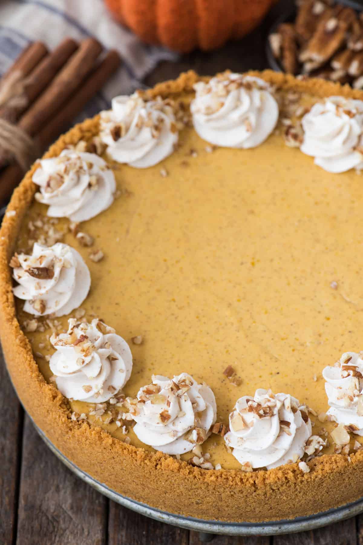 whole pumpkin cheesecake with whipped cream swirls and chopped nuts on wooden background