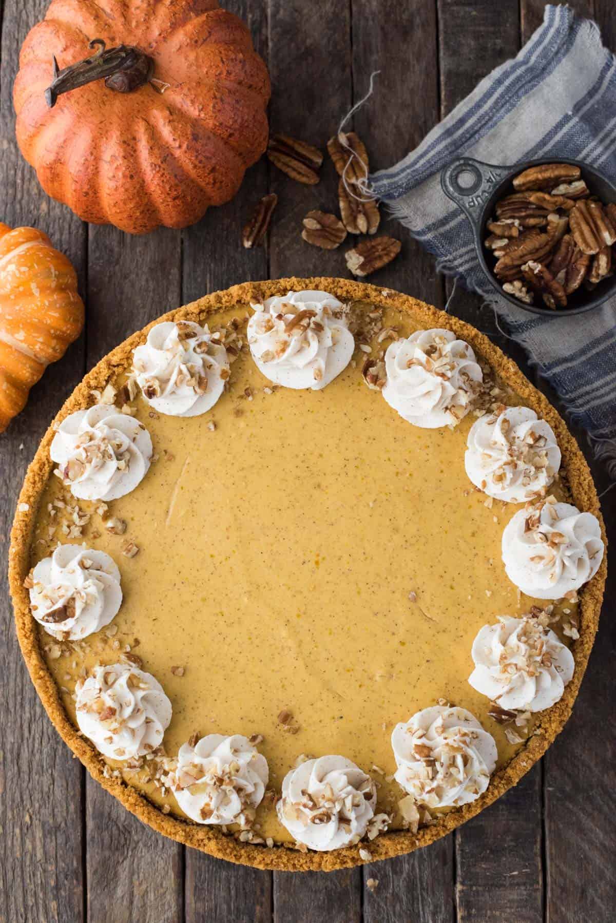 whole pumpkin cheesecake with whipped cream swirls and chopped nuts on wooden background