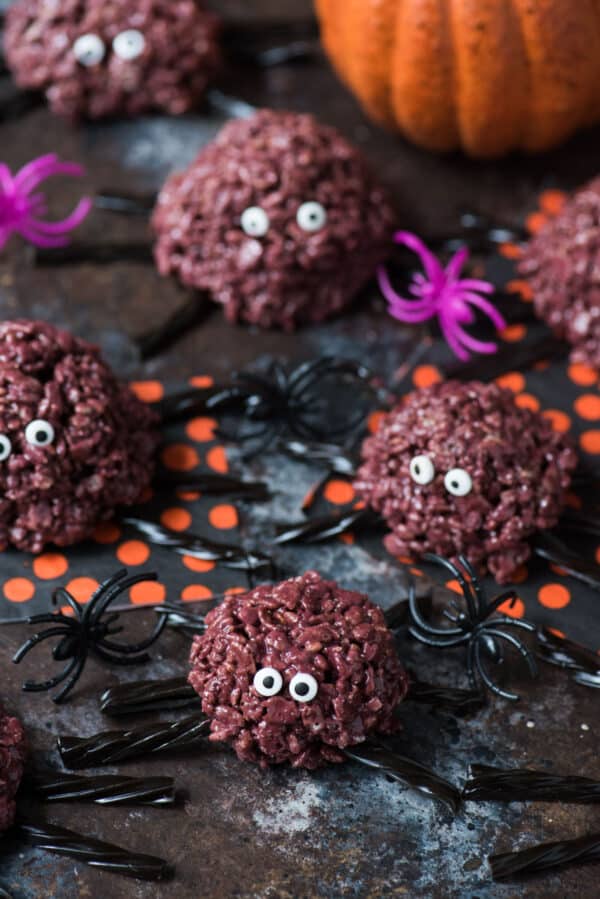 purple spider rice krispie treats with black licorice legs on a dark background