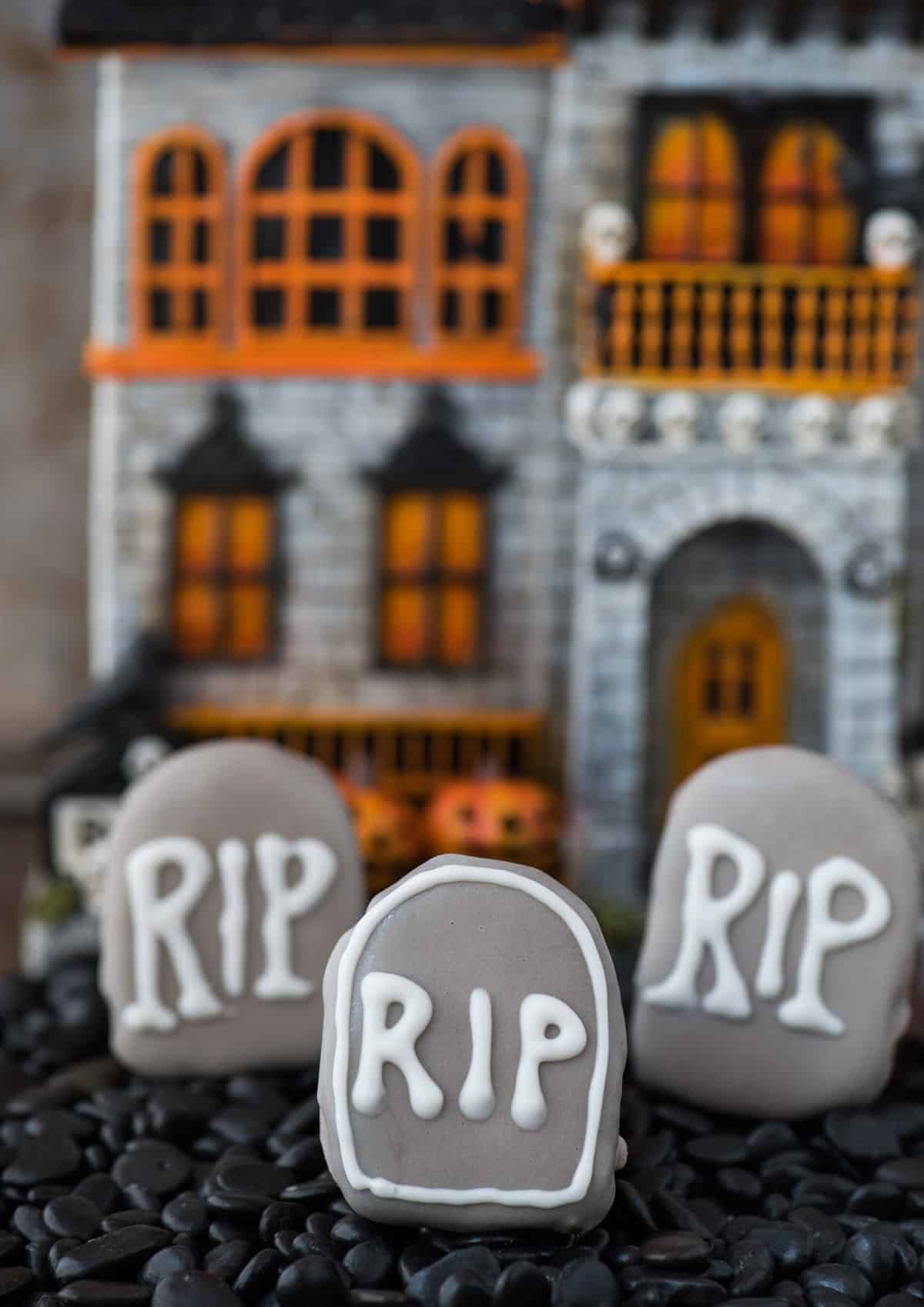 tombstone shape oreo balls in shallow pan surrounded with black rocks with haunted house in the background