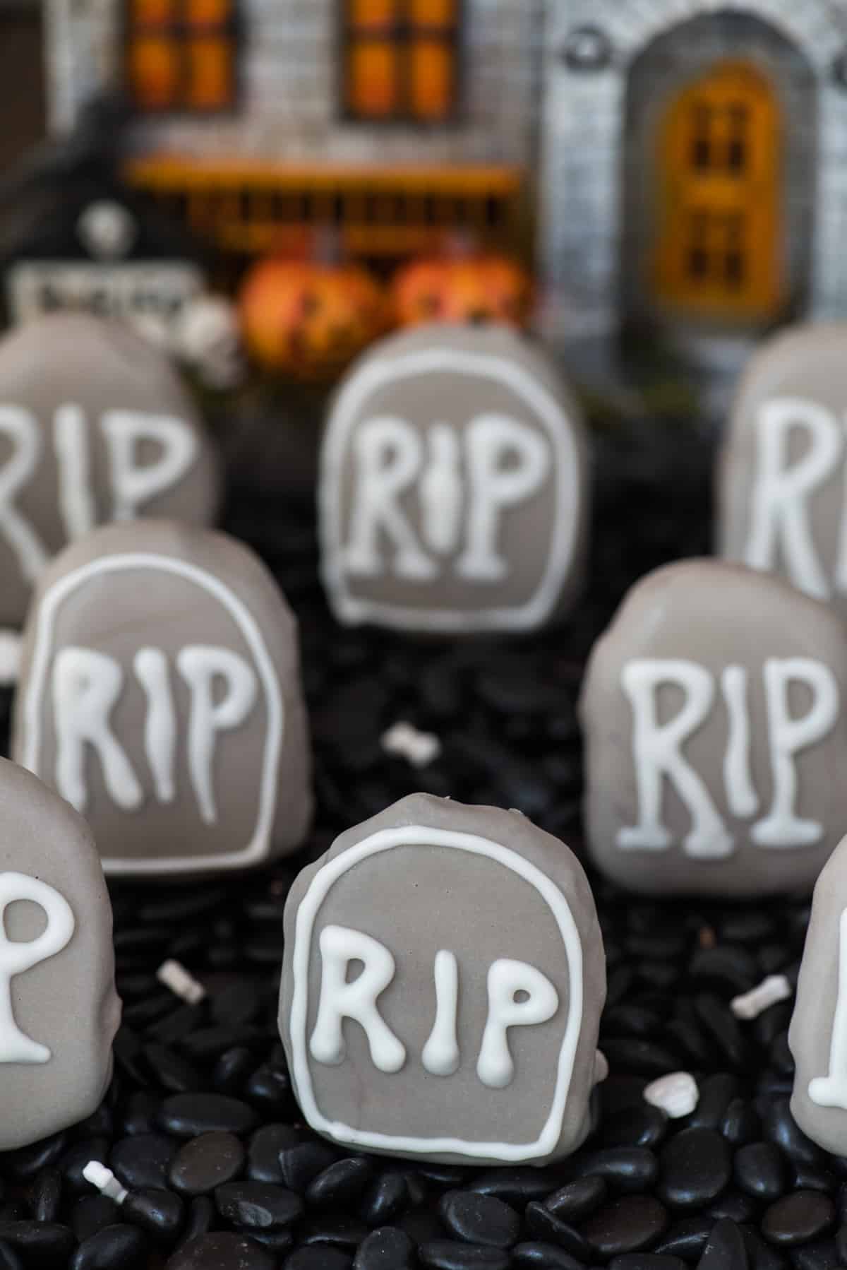 tombstone shape oreo balls in shallow pan surrounded with black rocks with haunted house in the background