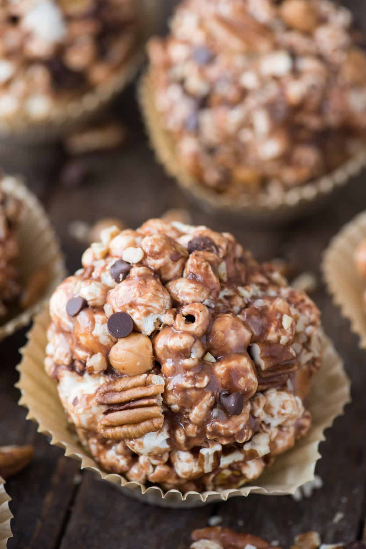 turtle popcorn balls with caramel, chocolate and pecans in paper liner on dark wood background