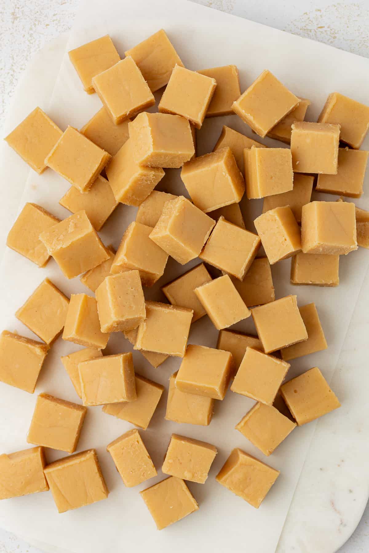 peanut butter fudge cut into small squares arranged on white parchment paper 