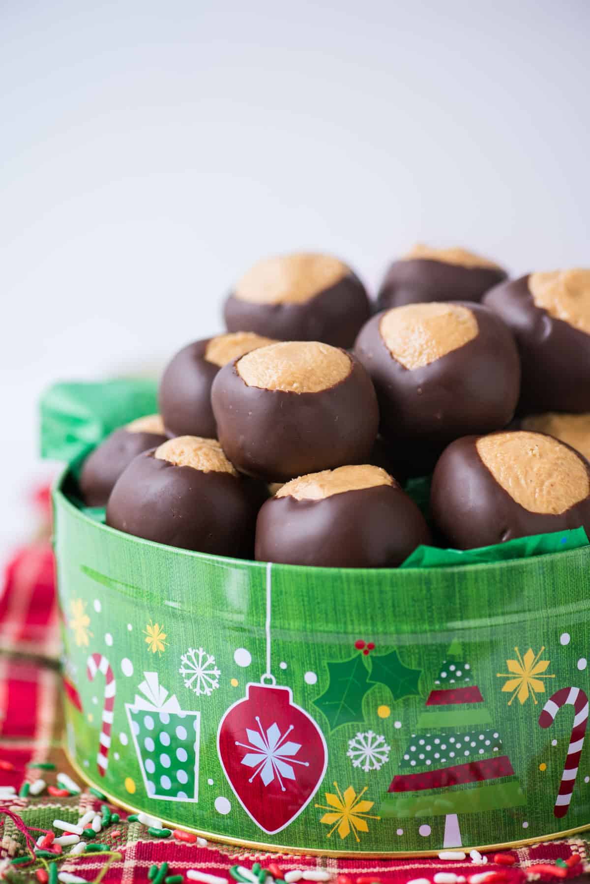 peanut butter balls in green christmas cookie tin with red striped towel under the tin