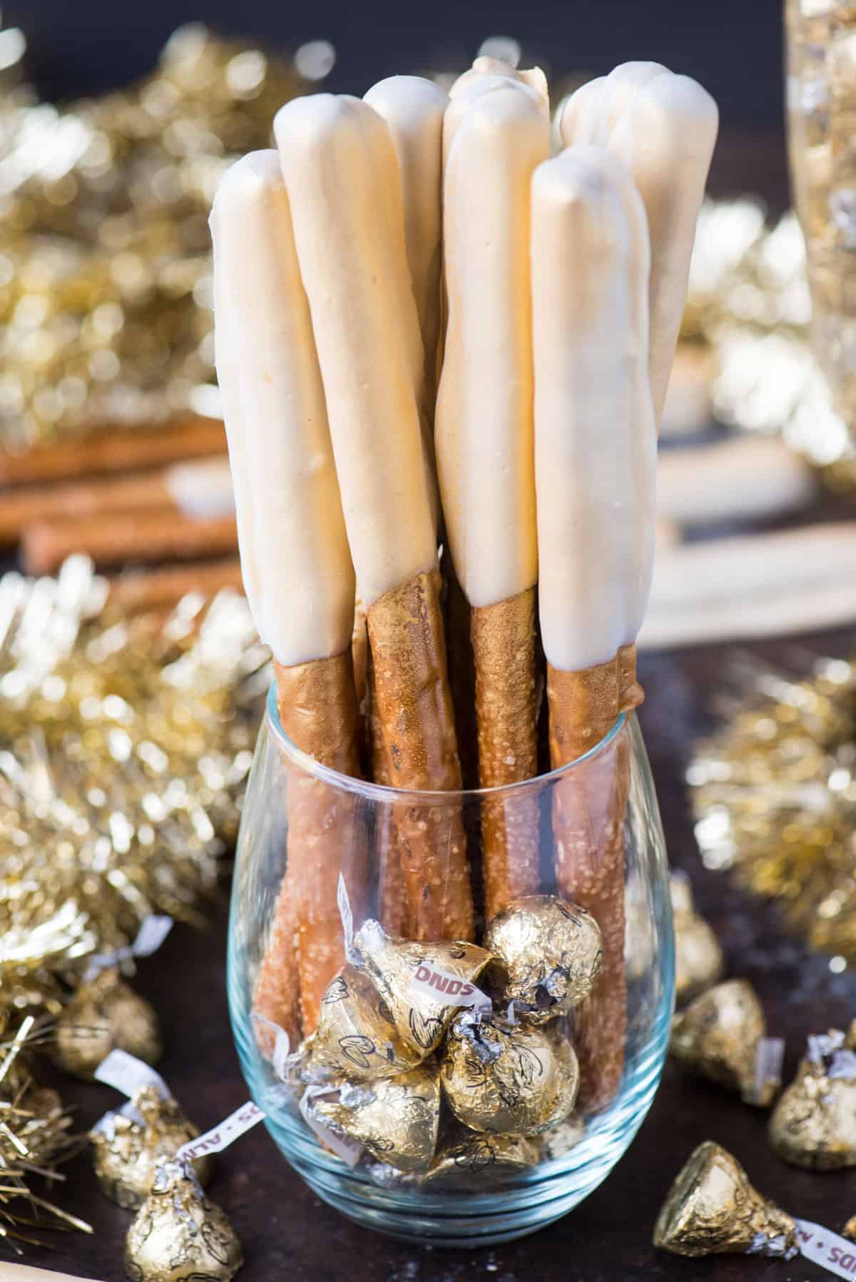 pretzel rods dipped in caramel and white chocolate and sprayed with edible gold paint to look golden and shimmery in a glass clear