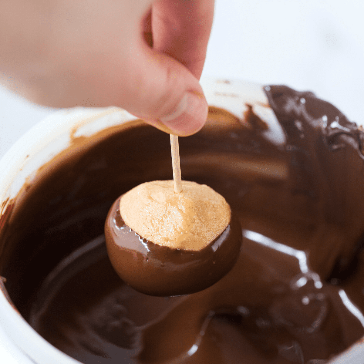 hand dipping peanut butter ball into melted chocolate using a toothpick