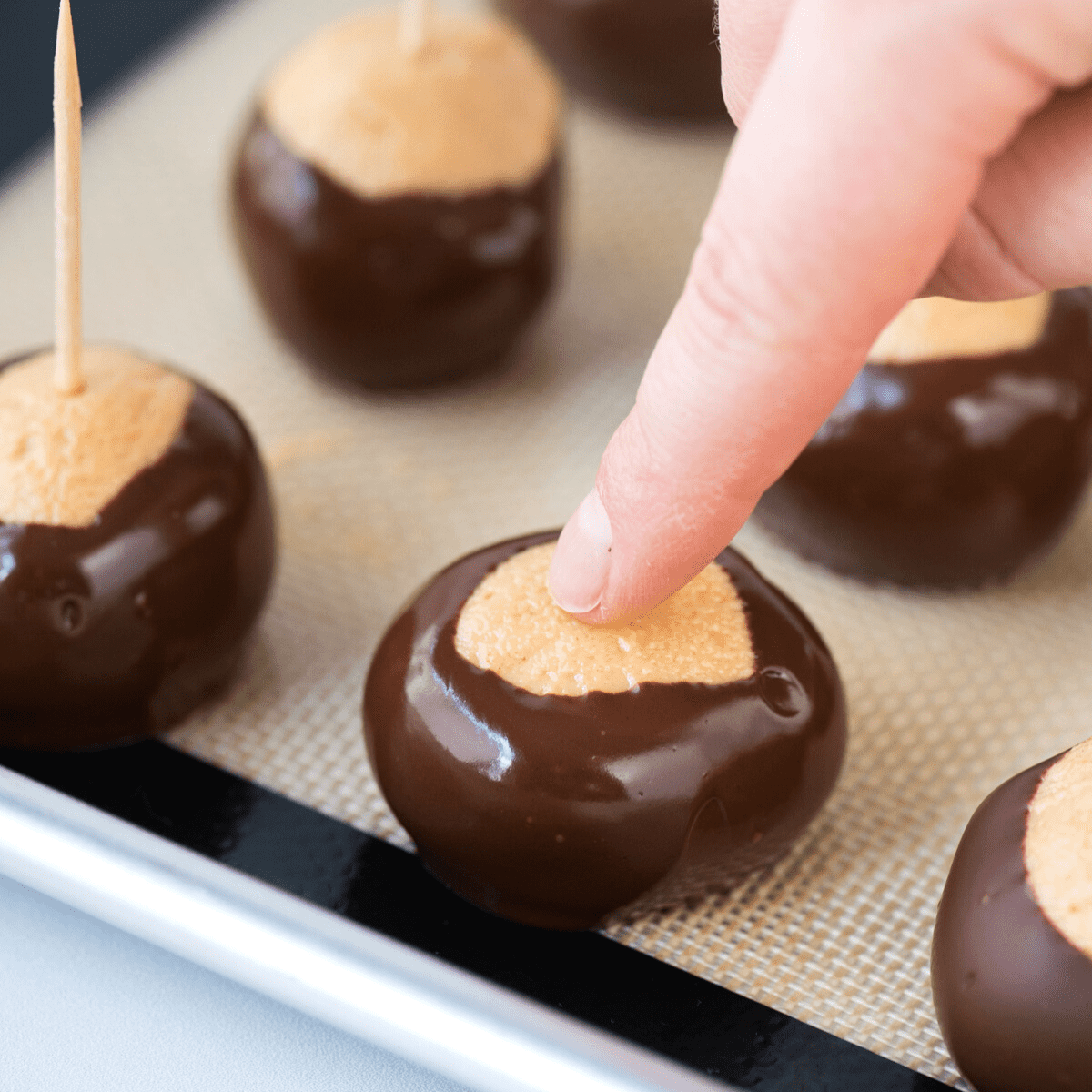 peanut butter ball freshly dipped in chocolate with finger covering the hole from the toothpick 