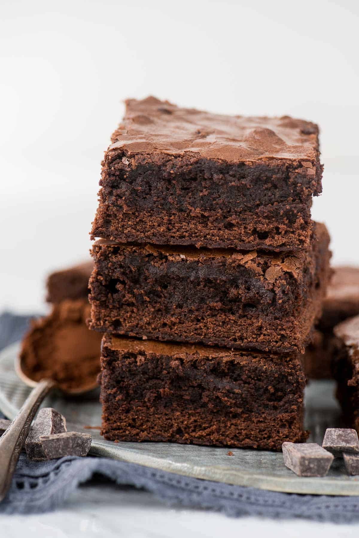 3 brownies in a stack on gray plate with blue linen underneath 