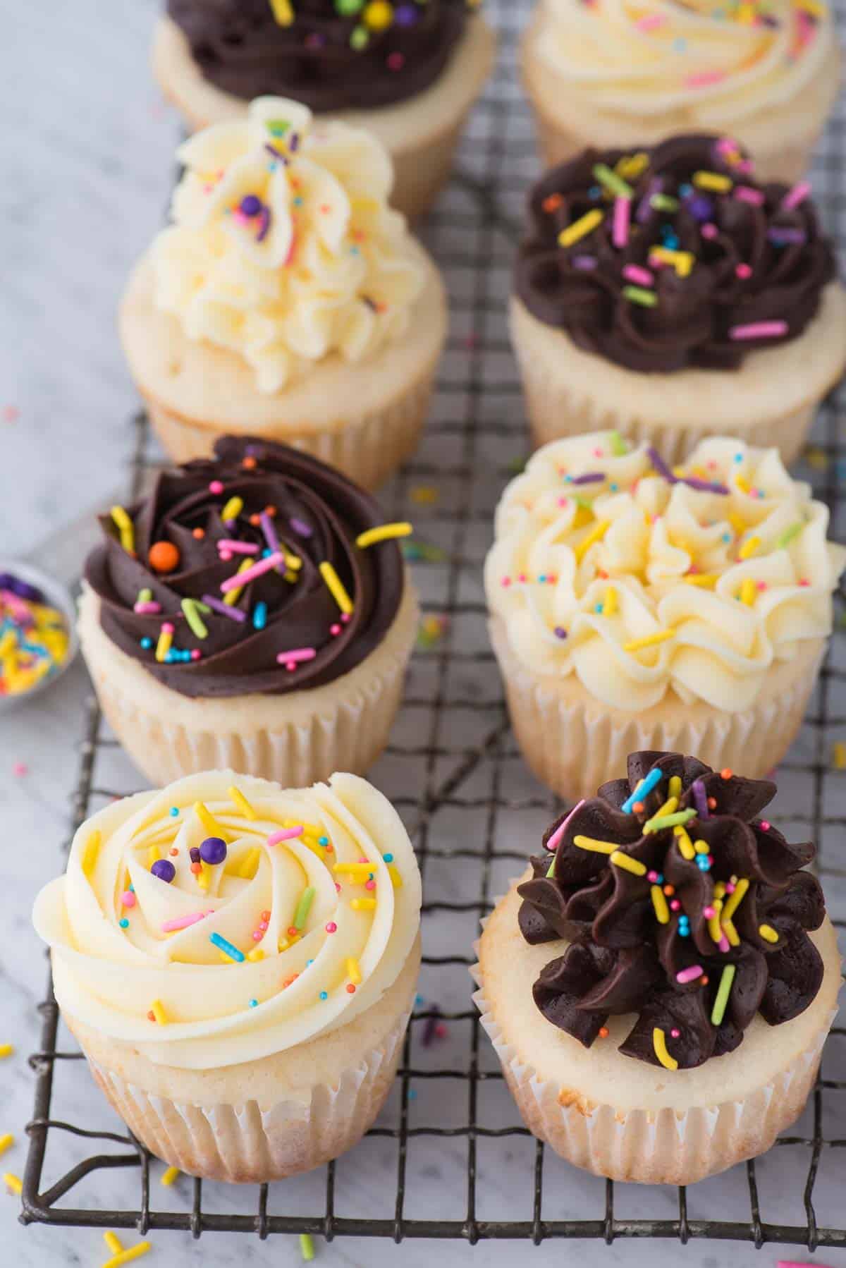 easy white cupcakes with chocolate or vanilla frosting with colorful sprinkles on wire cooling rack