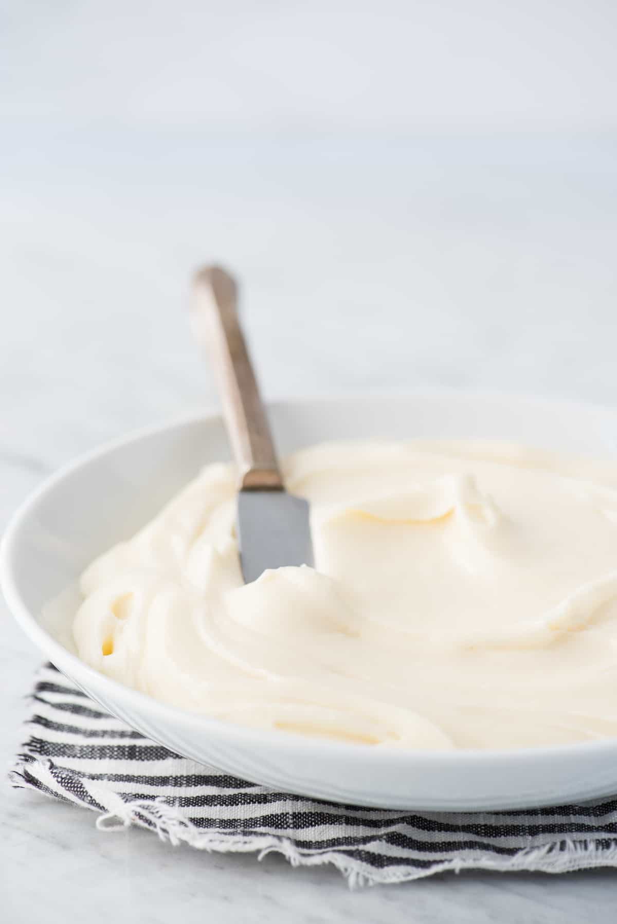 cream cheese frosting in white bowl with metal knife in bowl