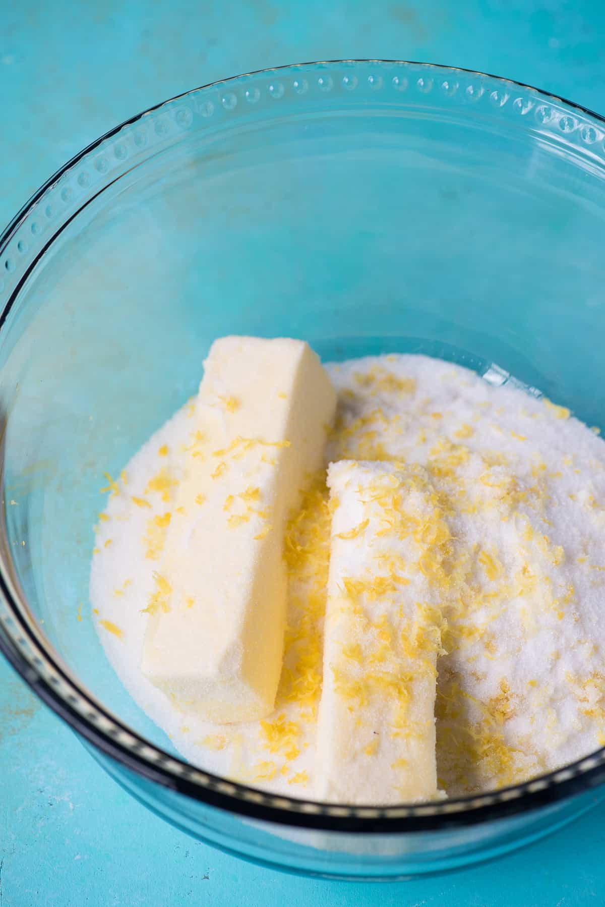 butter, granulated sugar and lemon zest in a glass bowl on blue background