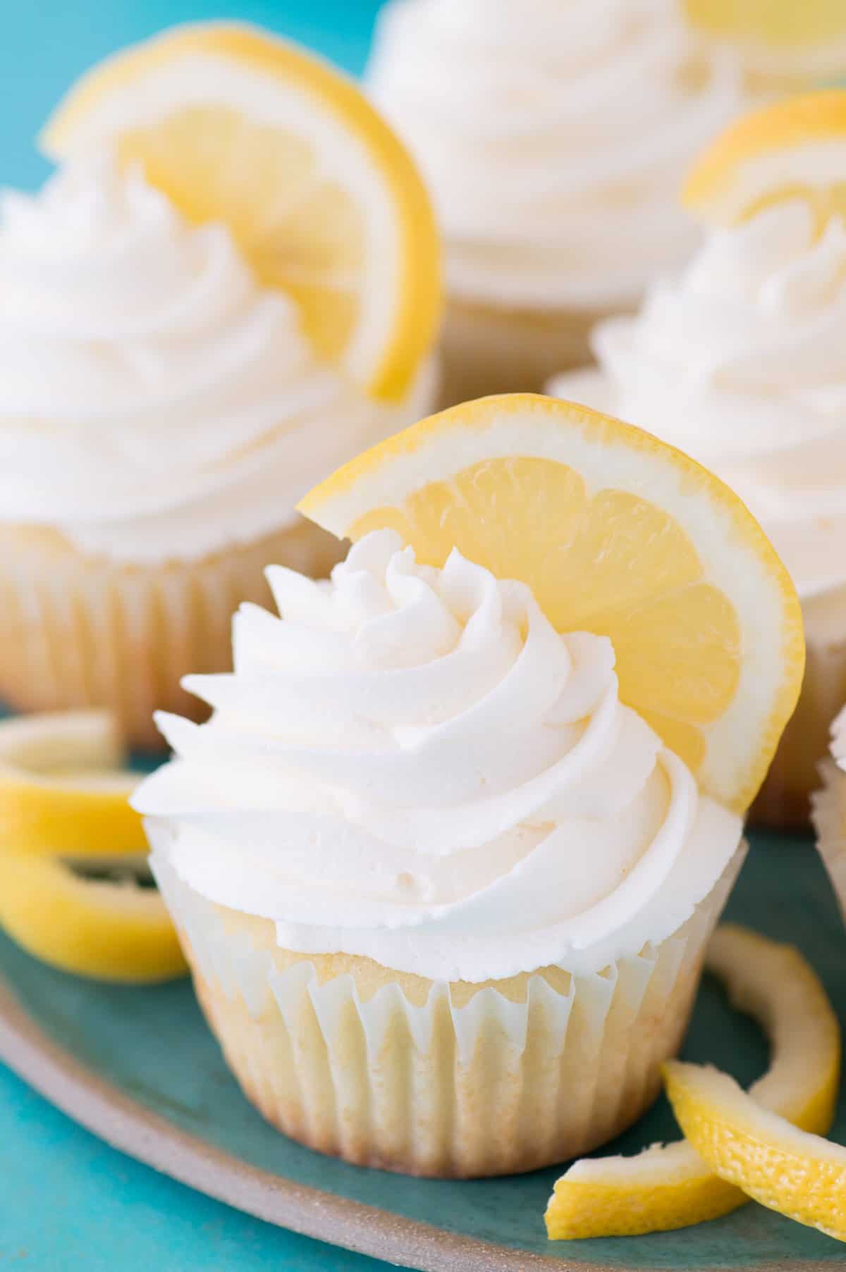 lemon cupcakes piped with lemon frosting and a lemon wedge on a teal plate and teal background