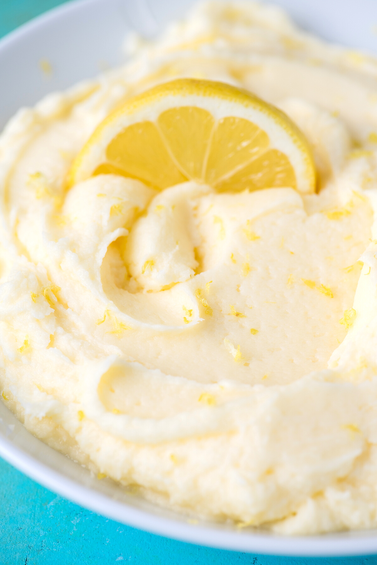 lemon frosting in a bowl white topped with a lemon slice